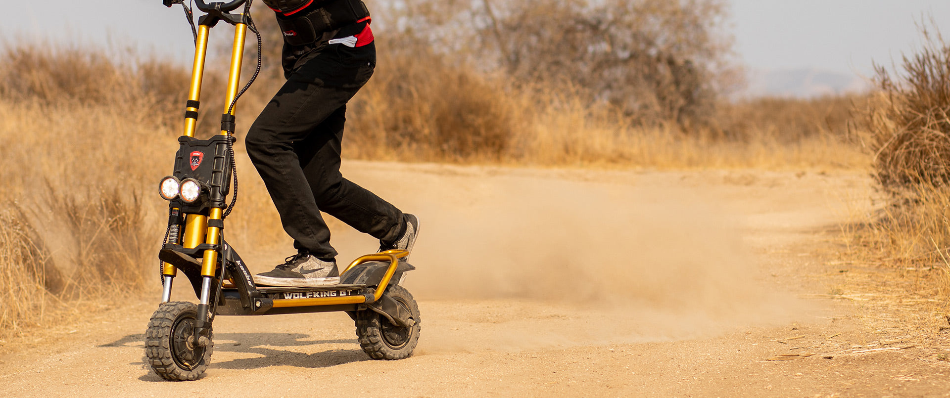 Action shot of a rider on a Kaabo Wolf King GT Pro electric scooter navigating an off-road trail, with dust swirling behind, highlighting the robust performance and adventure-ready design of the scooter.
