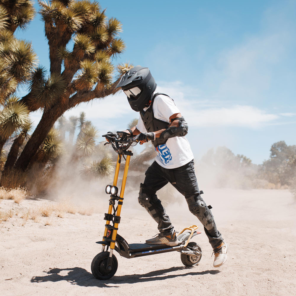 Rider wearing protective gear riding the Kaabo Wolf Warrior X Max electric scooter on a dusty off-road trail