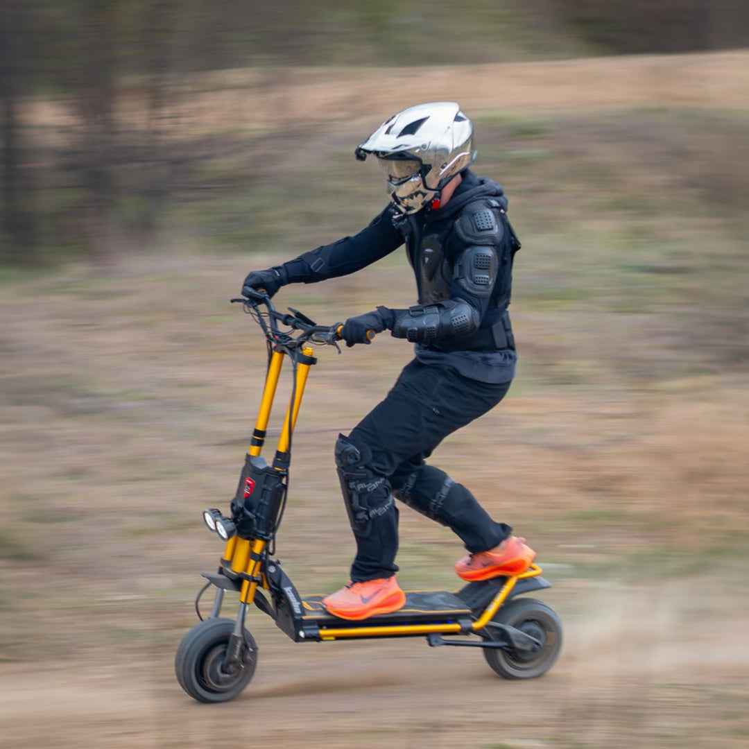 A person riding an electric scooter on a dirt path, wearing a white helmet, black protective gear, and bright orange shoes.