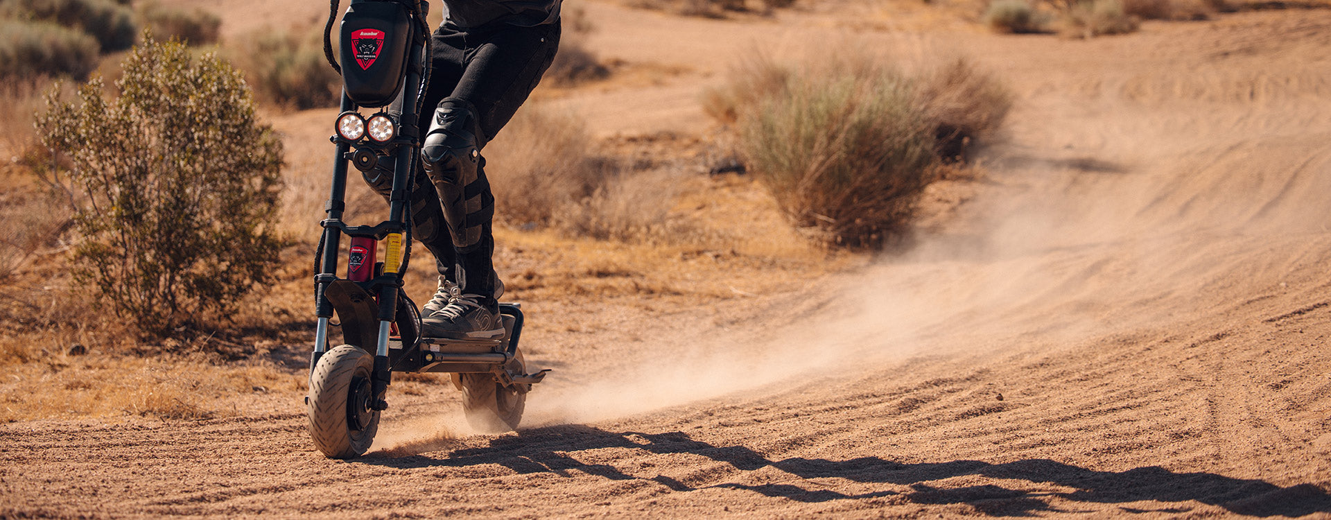 An electric scooter rider navigating a dusty trail on the Kaabo Wolf Warrior 11 Pro+ with a desert landscape in the background, highlighting the scooter's off-road capabilities.