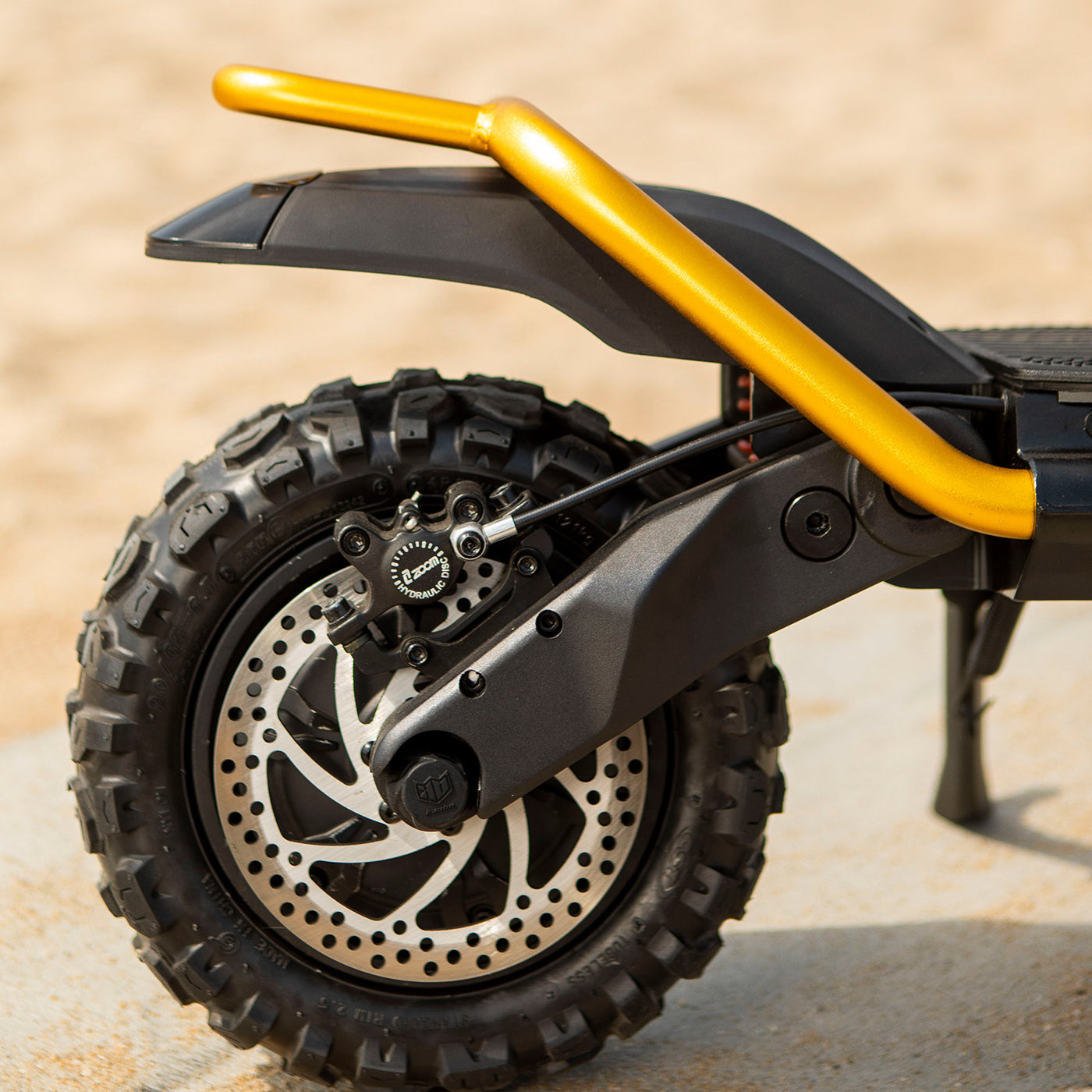 A close-up view of the Kaabo electric scooter's rear wheel, showing the intricate disc brake system, off-road tire, and the suspension with yellow accents.
