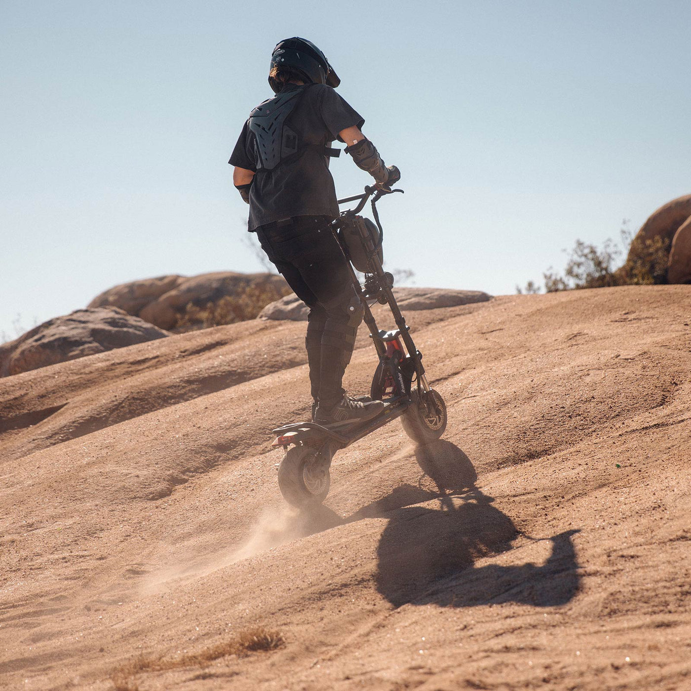 Rider conquering a steep hill with the Kaabo Wolf Warrior 11 Pro+ electric scooter, showcasing its impressive hill-climbing ability and durable design in a rugged outdoor setting.