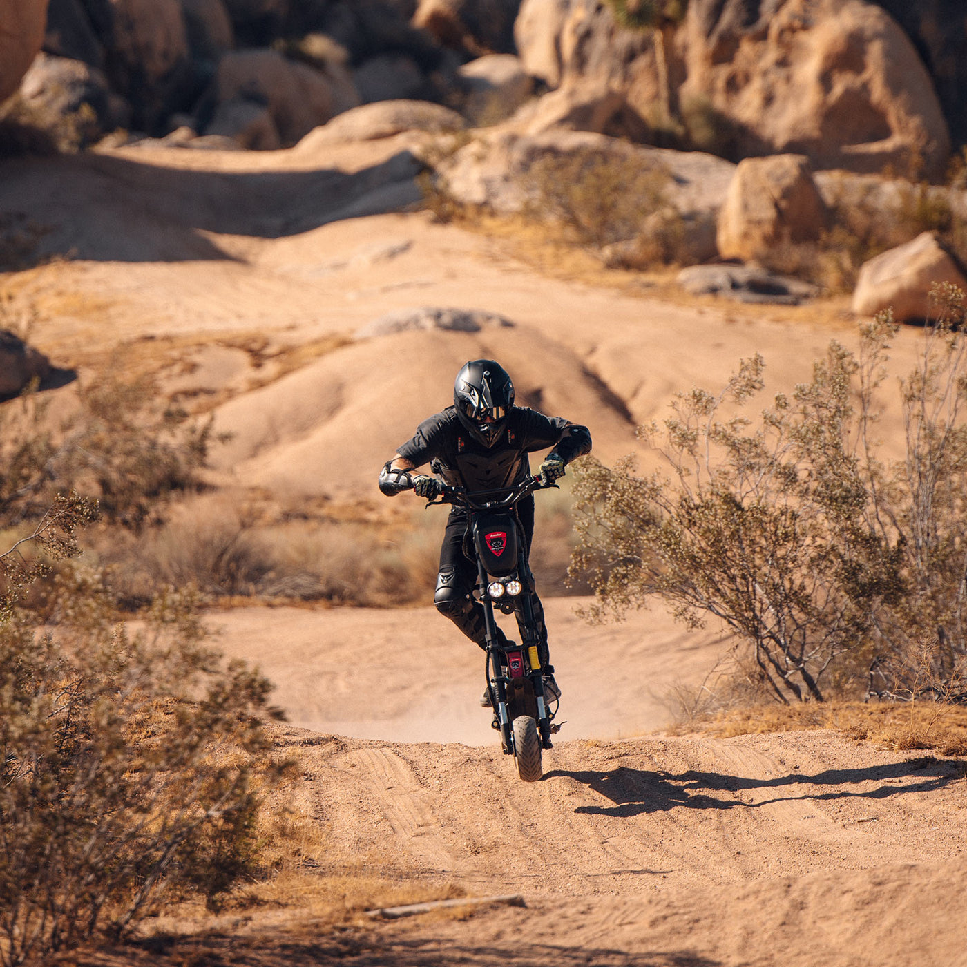 A rider on a Kaabo Wolf Warrior 11 Pro+ electric scooter catching air over a desert trail, demonstrating the scooter’s off-road capabilities and high performance.