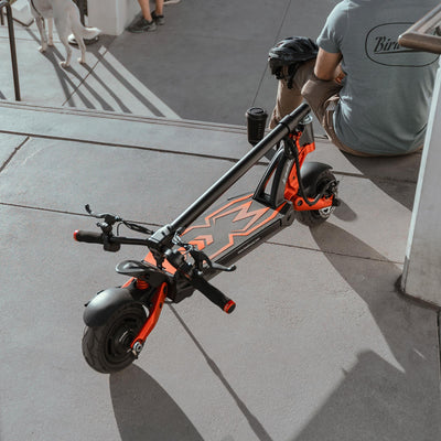 Kaabo Mantis 8 electric scooter leaning on a sidewalk railing near a café, epitomizing the ease of integrating e-scooters into daily urban commuting
